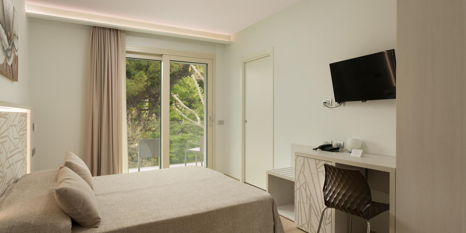 Camera moderna con letto, TV e balcone vista natura.