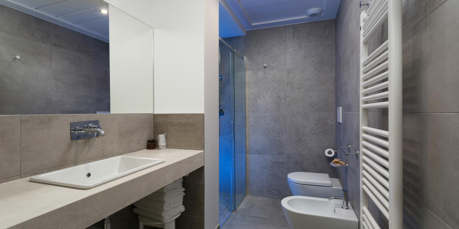 Bagno moderno con doccia, lavabo, bidet e termosifone.