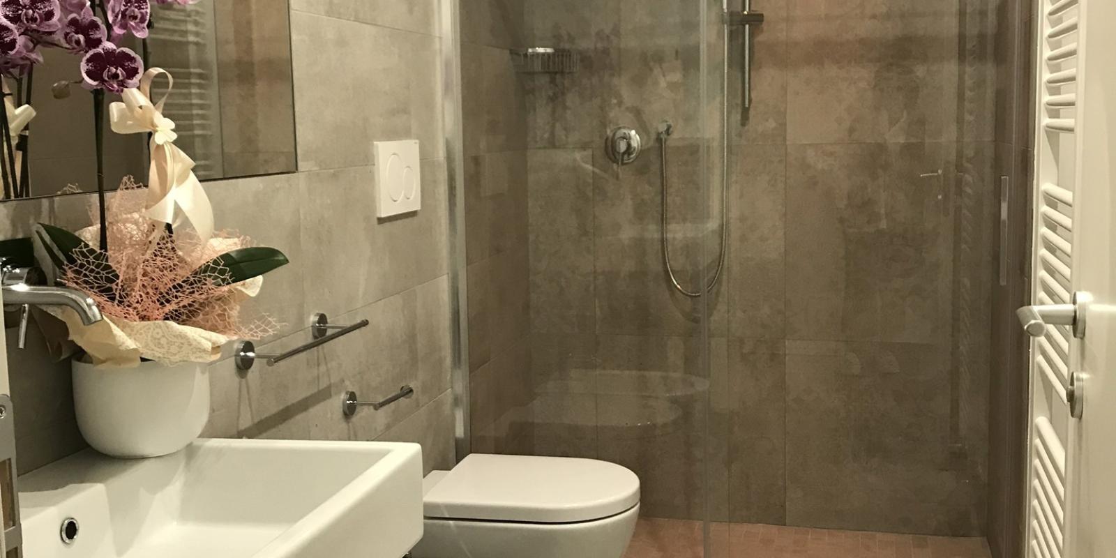 Bagno moderno con doccia, lavandino, WC e pianta decorativa.