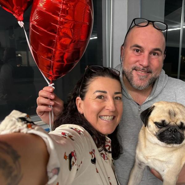 Coppia felice con cane e palloncini rossi a cuore.